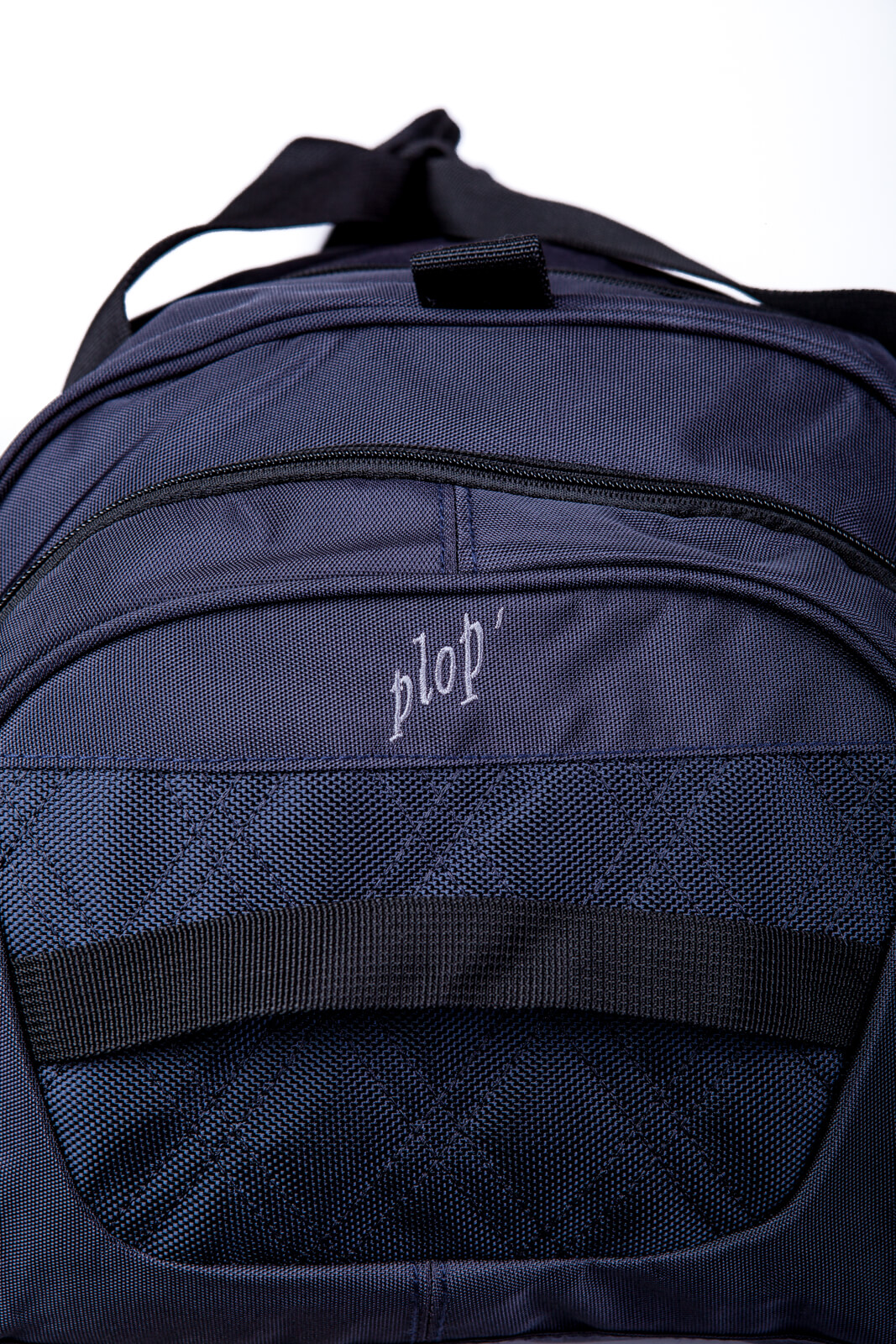 Detailsansicht der kurzen Seite einer blauen Sporttasche mit geprägtem Schriftzug „plop’“ auf der Außentasche. Die Tasche zeigt einen schwarzen Tragegriff und einen Reißverschluss oben.