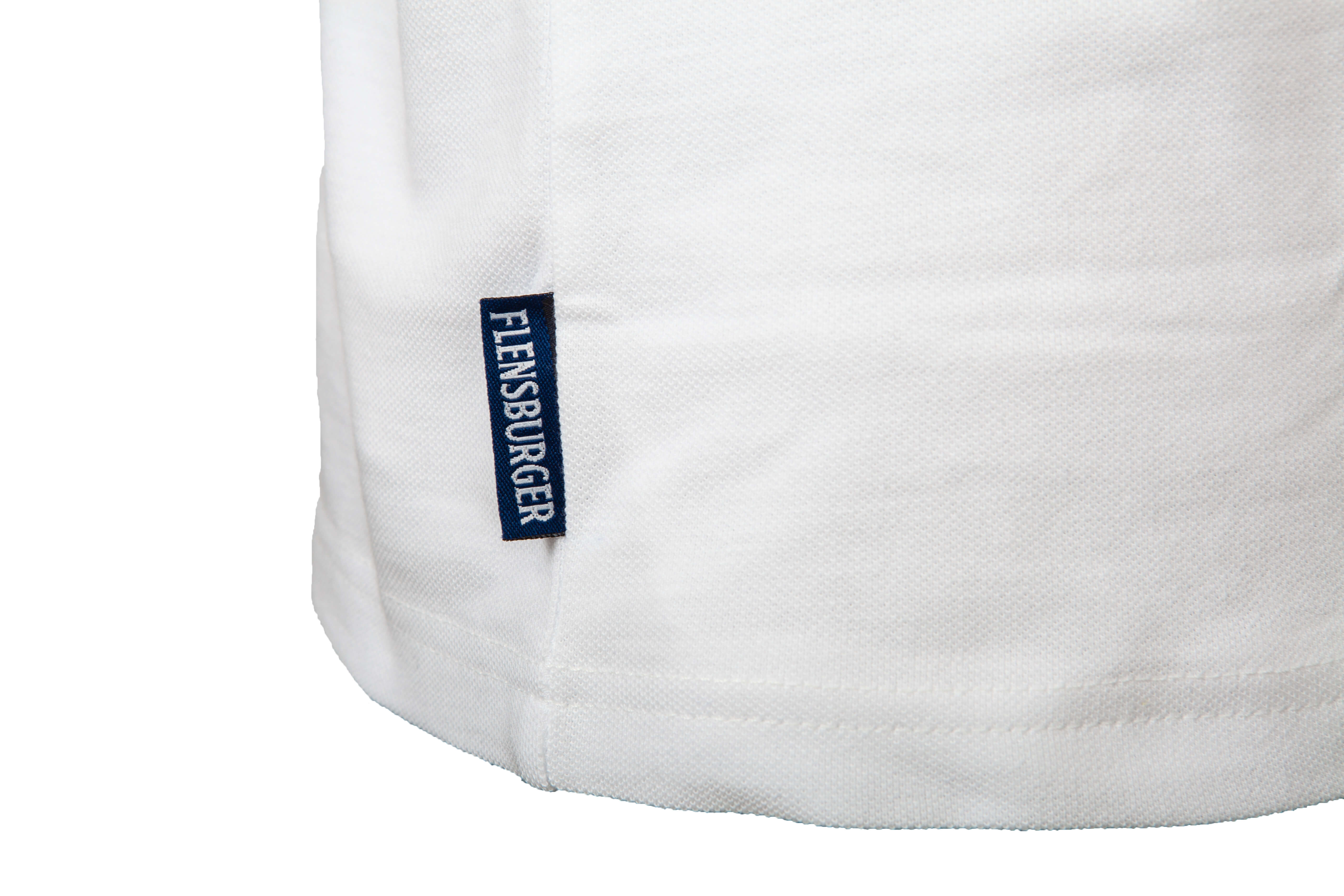 Detailansicht des unteren Teils eines weißen Baumwoll-Poloshirts mit einem blauen Etikett, auf dem „FLENSBURGER“ steht.