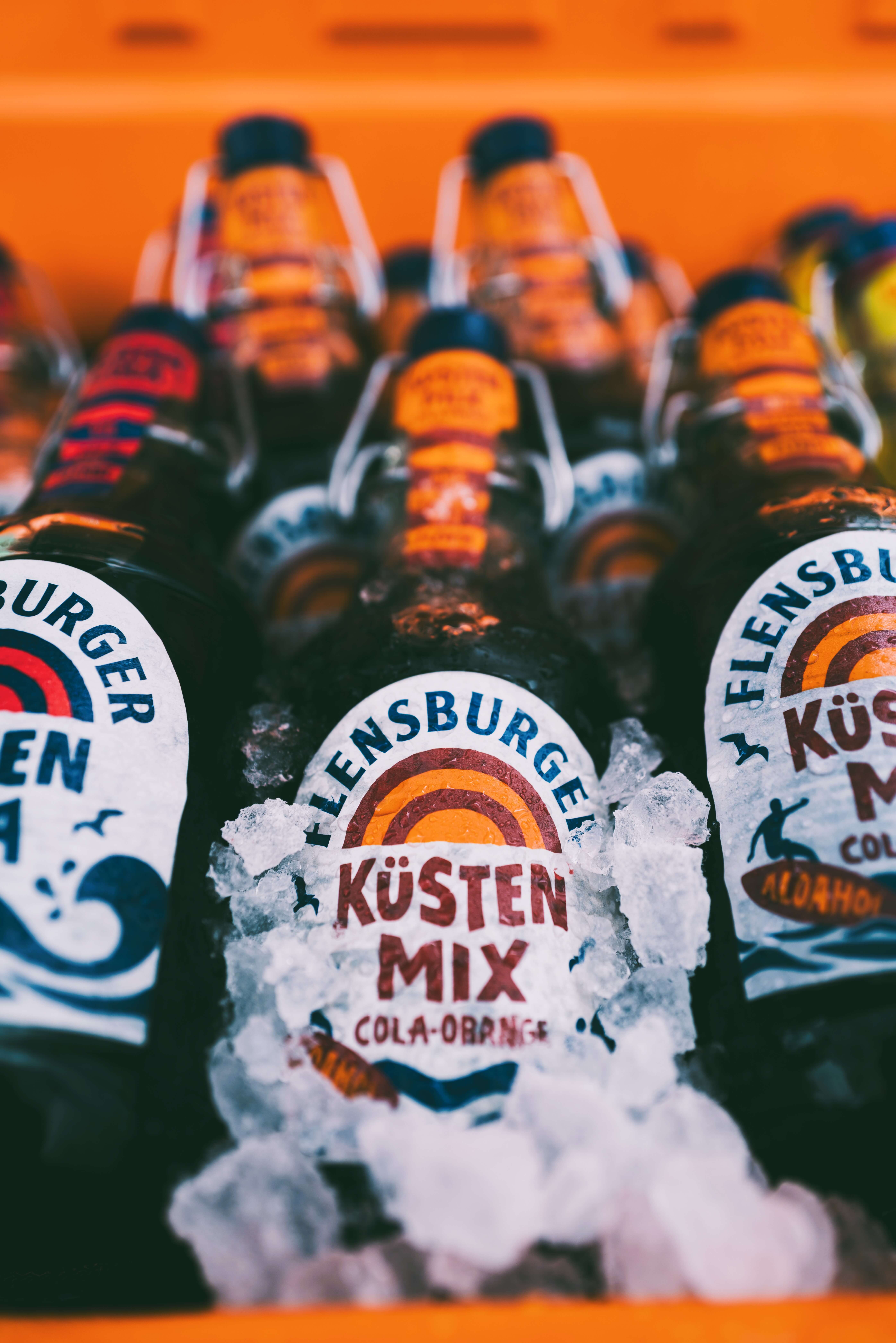 Flensburger Küstenmix "Cola-Orange" Flensburger Küstenmix "Cola-Orange" Flaschen liegen dekorativ auf Eis. Die Etiketten zeigen den Namen, den Alkoholgehalt von 0,0% und die Menge von 0,33 Litern an.