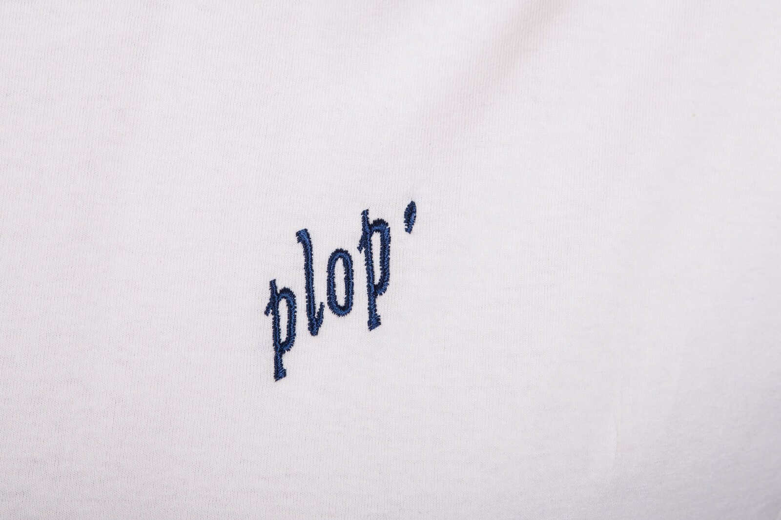 Weißer Stoff bestickt mit dem Wort "plop'" in navyfarbener Schrift.