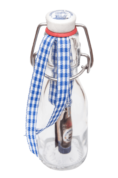 Eine Glasflasche mit einem Bügelverschluss. Am Bügel hängt ein blau-weiß kariertes Band. Im Inneren der Flasche ist eine kleine Flasche Bier. Der Flaschenverschluss zeigt ein blaues Logo mit Schriftzug.
