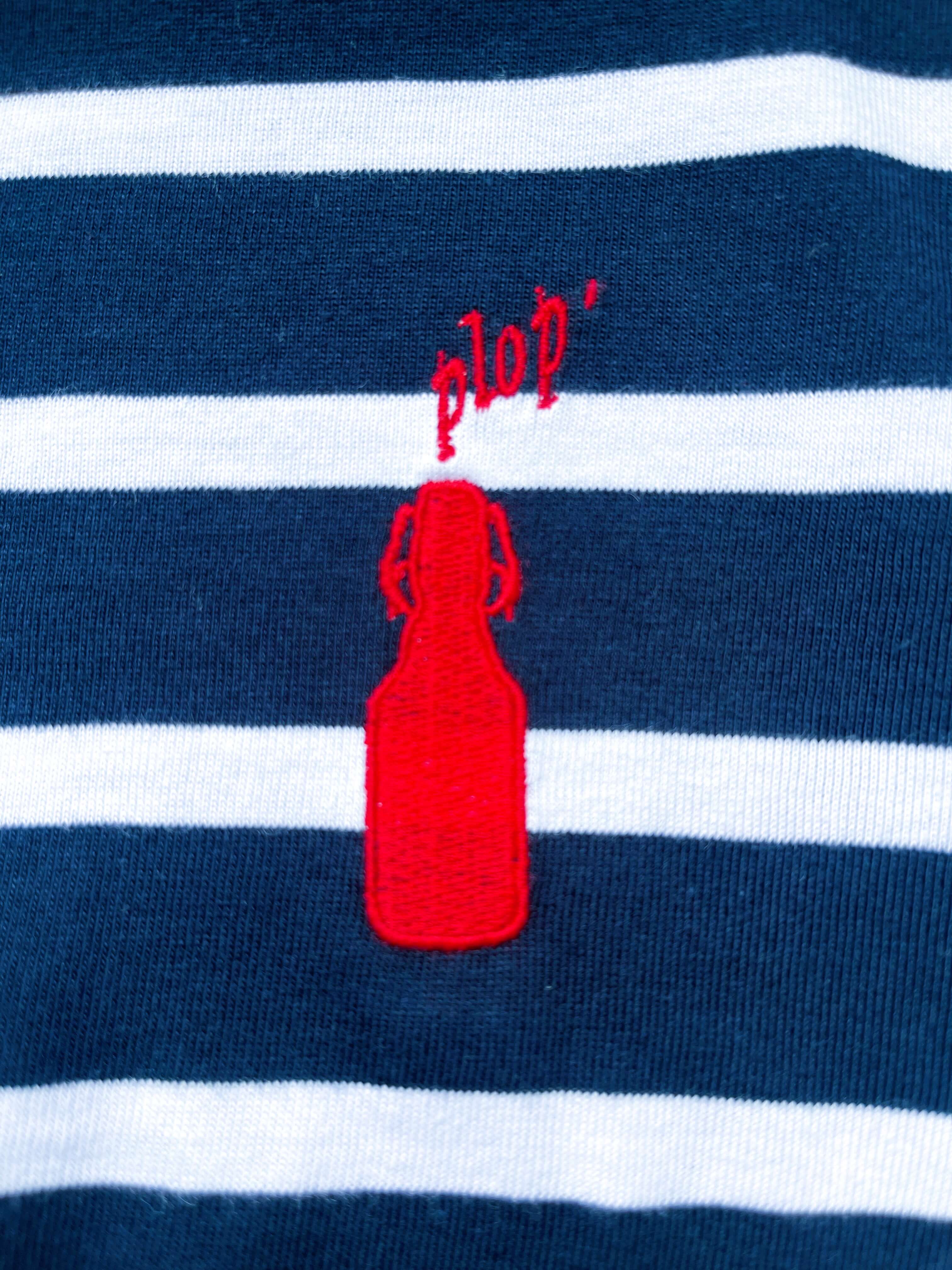 Rote, gestickte Flasche mit dem Schriftzug "plop’" auf blau-weiß gestreiftem Baumwollstoff eines Kurzarm-Shirts.