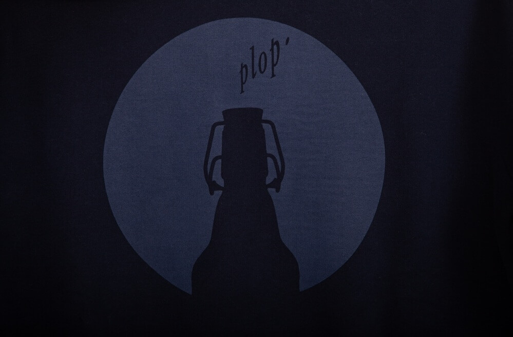 Dunkelblaue Flasche mit Bügelverschluss vor rundem hellblauem Hintergrund. Über der Flasche steht der schwarze Text "plop'".