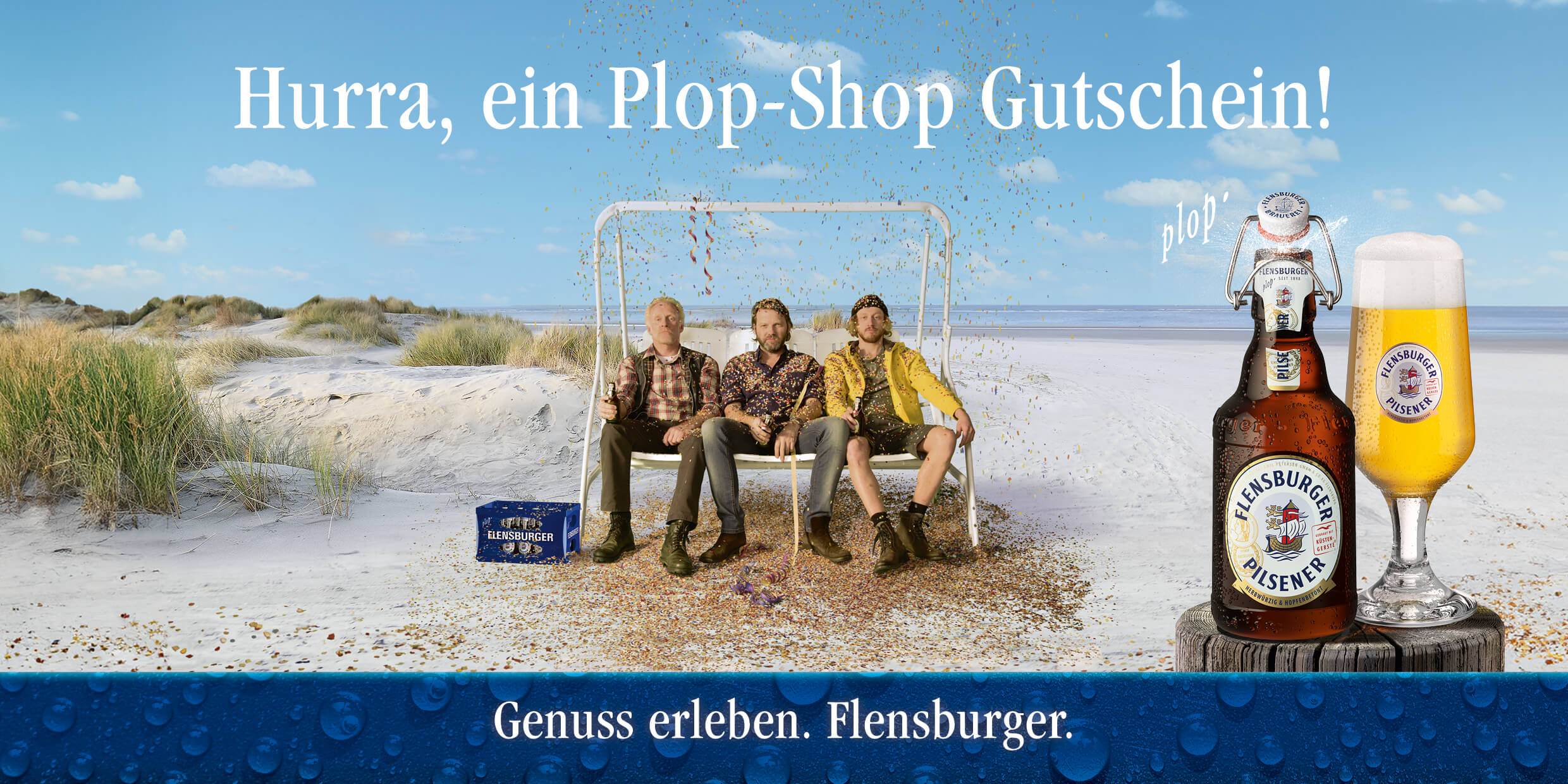 Drei Männer sitzen entspannt auf einer weißen Schaukel am Strand, während Konfetti in die Luft geschossen wird. Daneben stehen eine Flasche Flensburger Pilsener und ein gefülltes Glas auf einem Holzuntergrund.